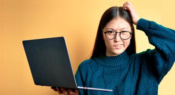 student holding laptop and looking confused