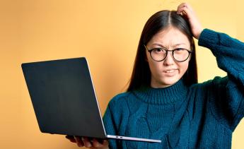 student holding laptop and looking confused