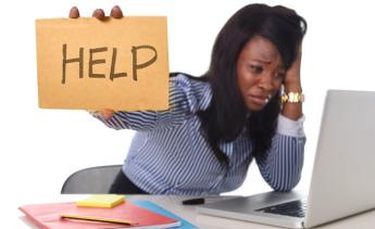 Woman holding "help" sign sitting at computer