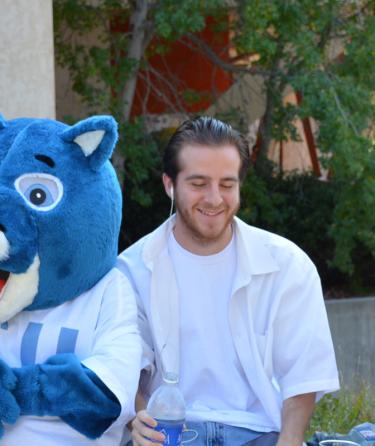 three students smiling with college mascot