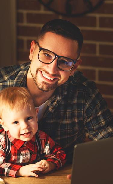 Father holding infant son while doing homework