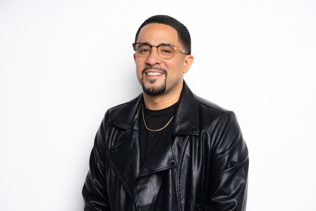 man in black shirt and jacket smiling and looking into the camera